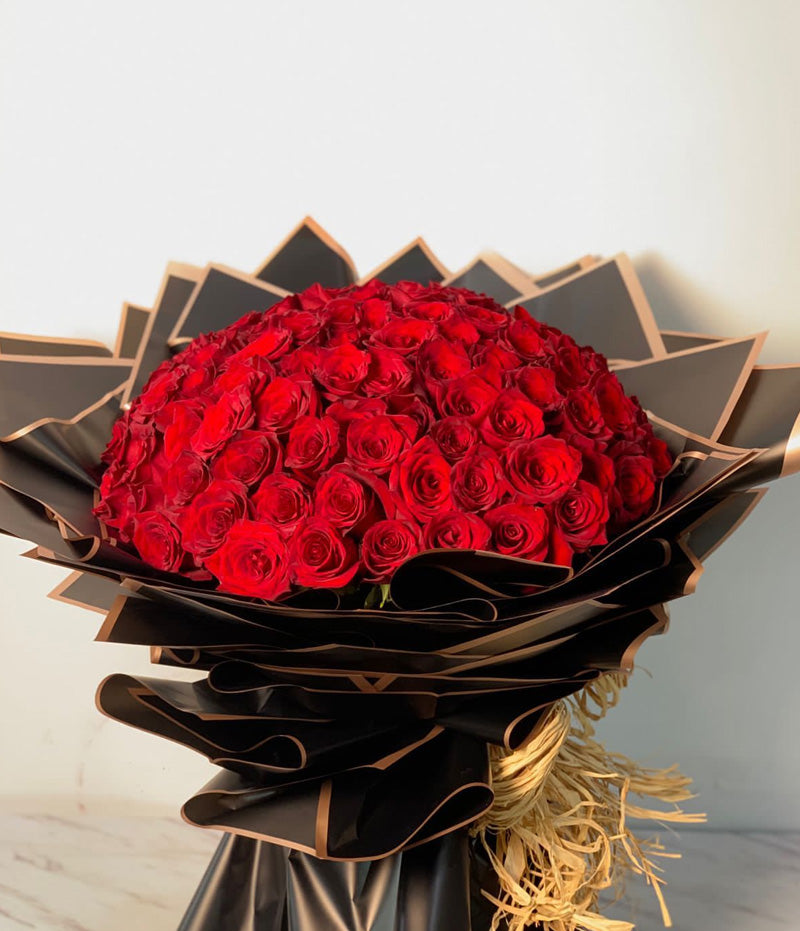 A bouquet of 100 red roses wrapped in black paper with a focus on the bright red petals.