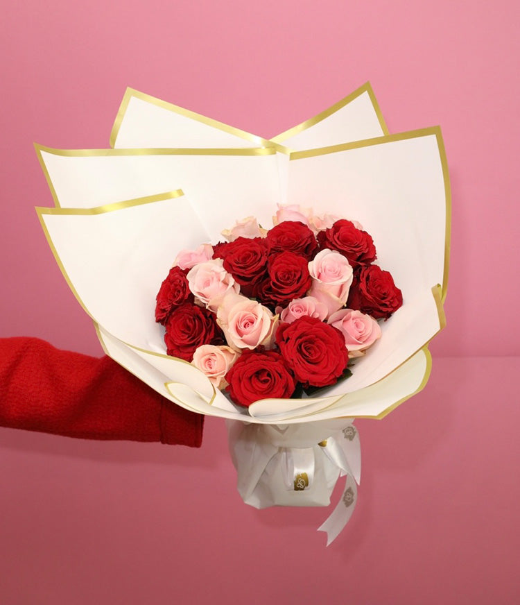 A paper-wrapped bouquet of red and pink roses set against a vibrant red background.