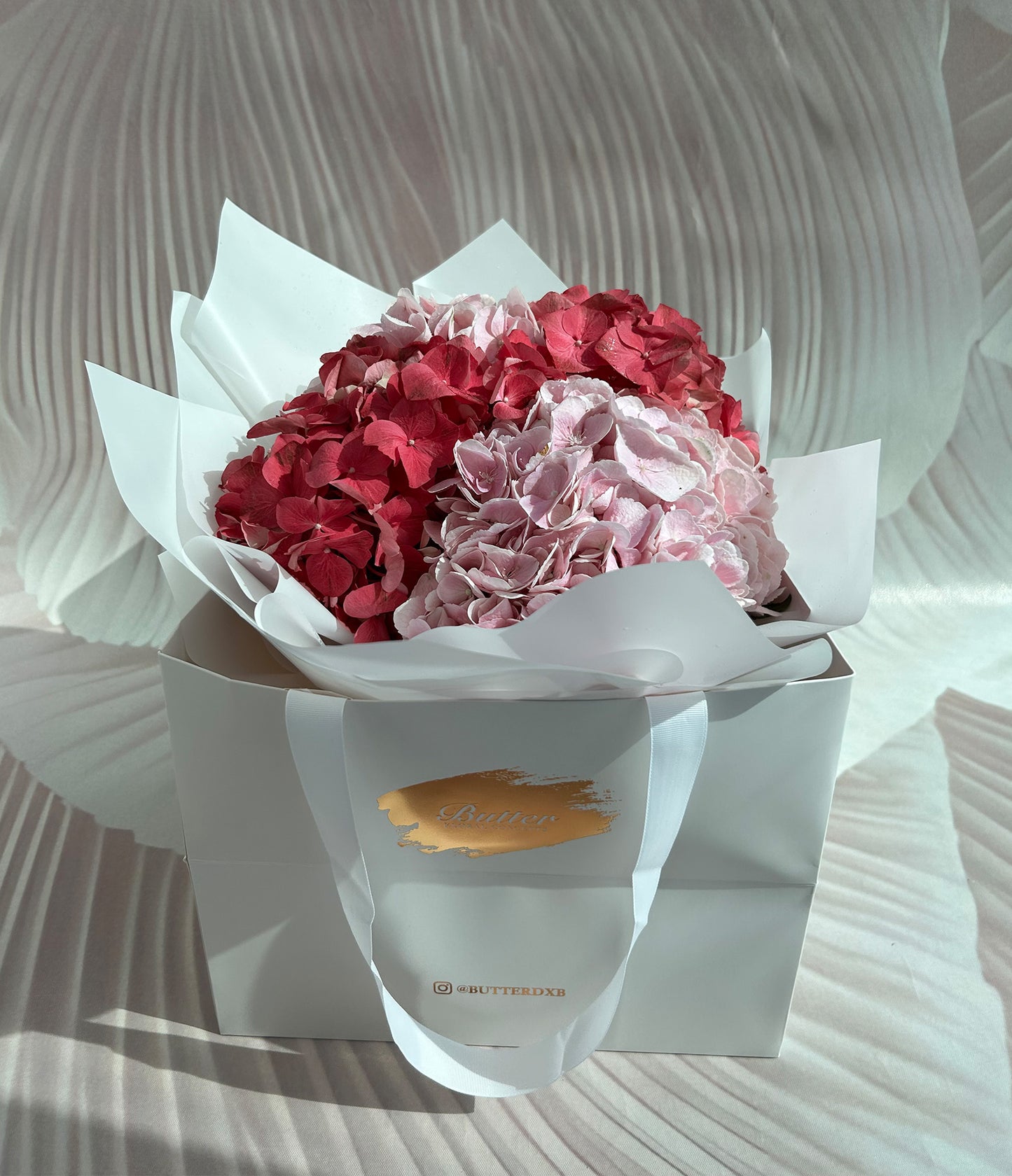 A beautifully arranged dome-shaped bouquet featuring pastel pink and dark pink hydrangeas. The flowers are densely packed, creating a full, lush appearance that exudes classic elegance and softness.