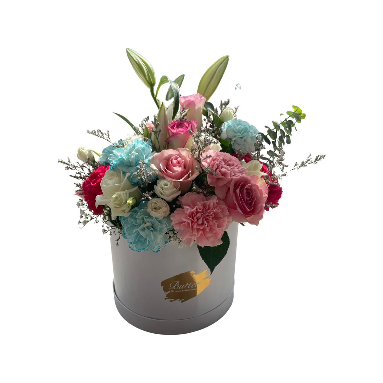 A round matte white box showcasing a bouquet of fresh flowers, including roses, baby roses, carnations, lilies, and lavender, all in gentle pastel shades.
