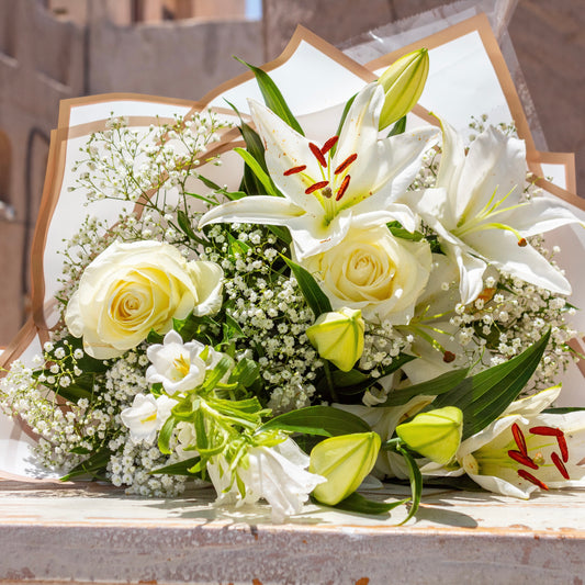 Close-up of Butter Bliss arrangement showcasing hand-picked white lilies and roses, tied and set against the matte white “Butter” bag.
