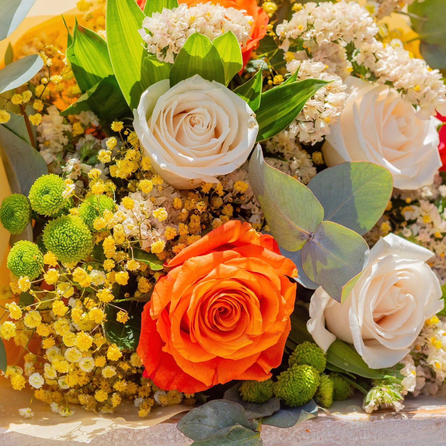 A closer angle that emphasizes a stunning orange rose surrounded by cream-colored blossoms and subtle greenery. This view captures the harmonious contrast and fresh, lively spirit of the arrangement.
