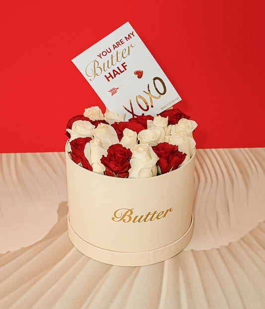 A beige hat box with the text 'BUTTER' on it, containing an arrangement of white and red roses and a gold-foiled card that reads 'You are my BUTTER half' with a kiss symbol 'xoxo'.
