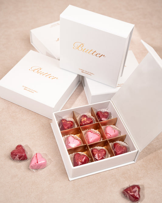 A white chocolate box containing various heart shaped chocolates with a rose ganache filling. The box is partially open, revealing the individually wrapped chocolates.