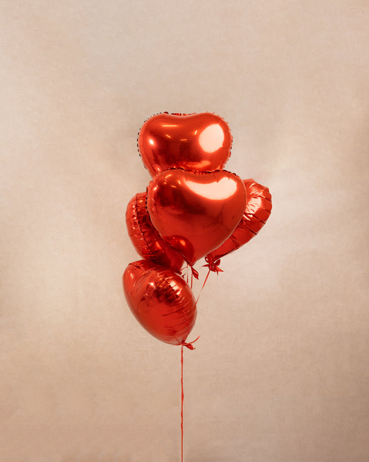 A bouquet of five red heart-shaped foil balloons arranged together against a neutral background.
