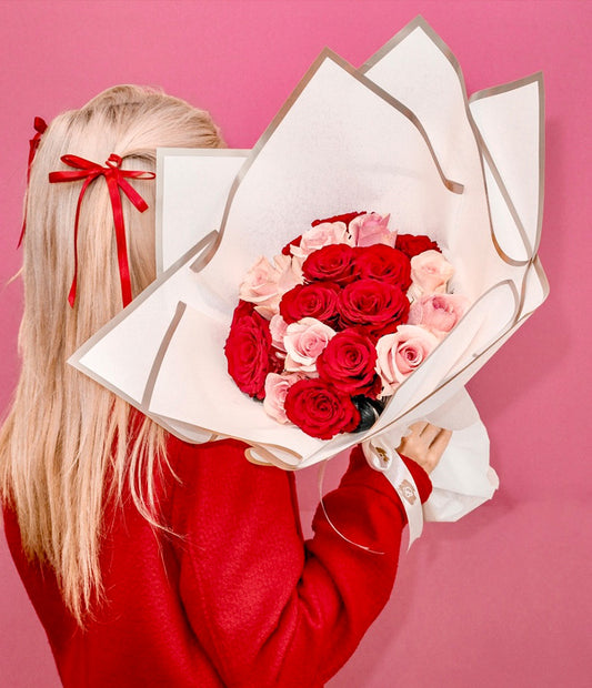 A bouquet of red and pink roses wrapped in paper, displayed against a red backdrop.