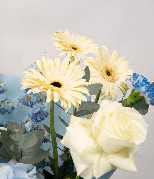 A close-up highlighting the mix of pearl-white blooms and muted aqua petals, complemented by fresh greenery for texture and depth.
