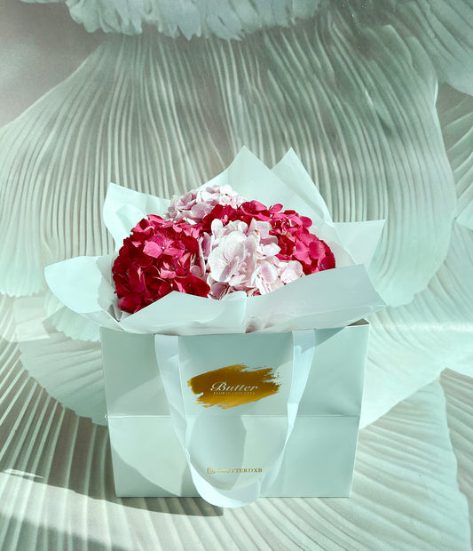 A bouquet of pastel pink and dark pink hydrangeas arranged neatly in a white wrapping with a gold logo. Fresh Hydrangea Dome!