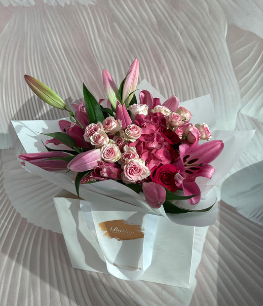 A radiant arrangement of lilies, hydrangeas, and roses in striking shades of pink. The flowers are artfully arranged and presented in a clean, elegant format perfect for a stylish gift or a beautiful home display.