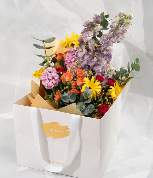 A close-up view of the Buttercup bouquet, highlighting the intricate details of the season's freshest hand-picked flowers. The arrangement features a blend of yellow, pink, and purple blooms, capturing the essence of joy and positivity. The vibrant colors and delicate petals are showcased in this detailed shot.