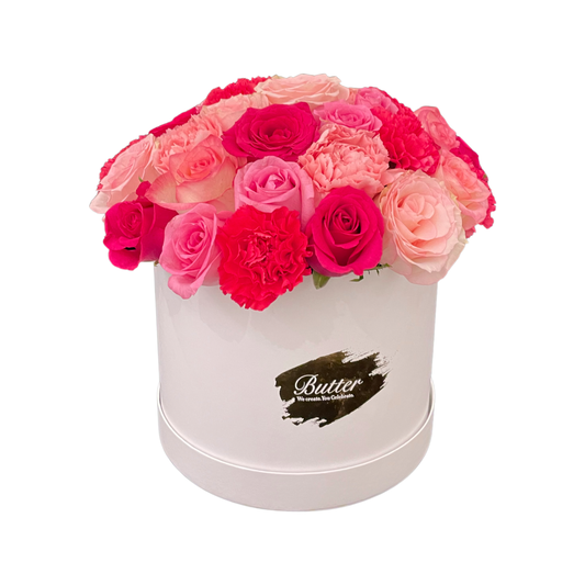 A round white hatbox with an assortment of blush pink flowers featuring roses and carnations.