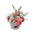A round matte white box containing an arrangement of fresh flowers including roses, baby roses, carnations, lilies, and lavender in a variety of pastel colors.