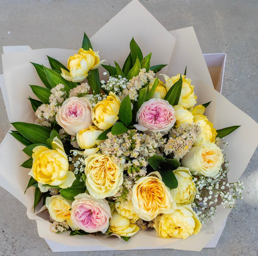 Charm floral arrangement with radiant yellow flowers displayed in a signature matte white Butter bag, offering a joyful yet elegant touch.